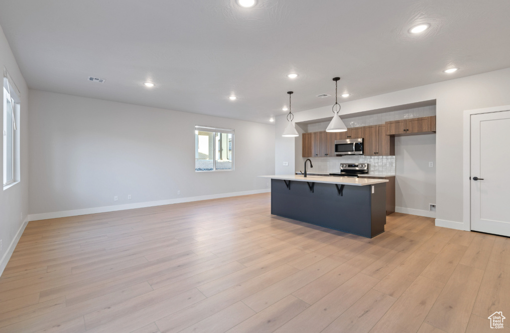 Kitchen with appliances with stainless steel finishes, brown cabinets, a breakfast bar area, light countertops, and recessed lighting