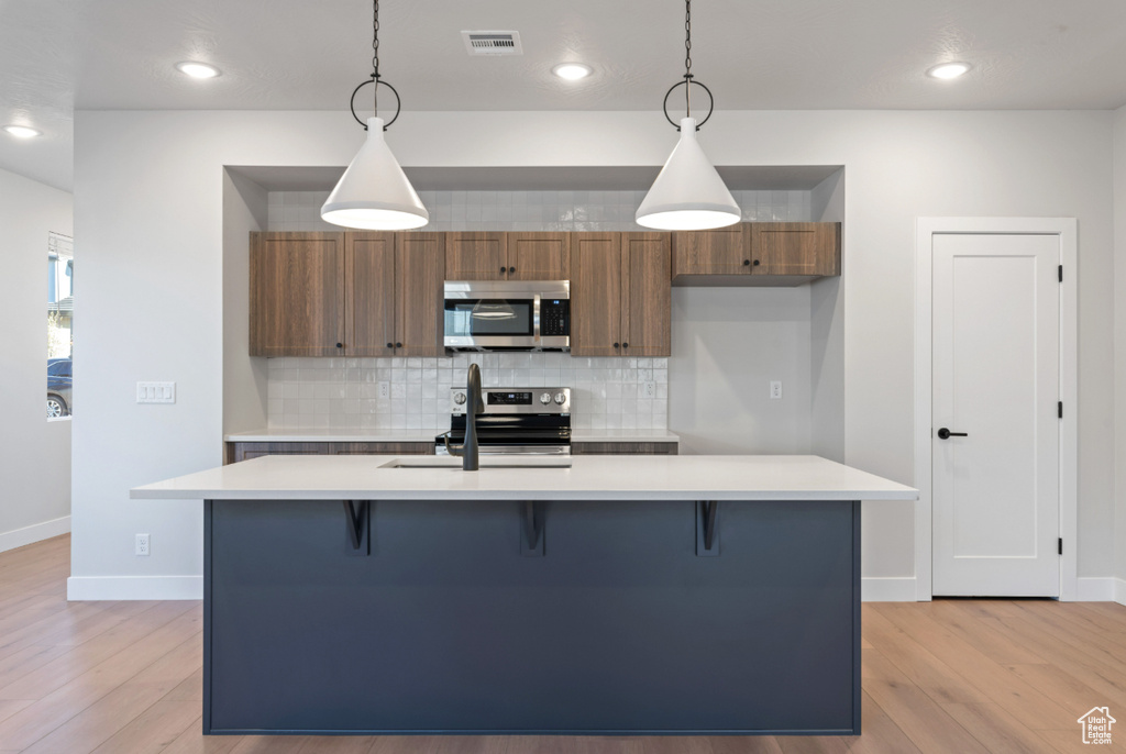 Kitchen with appliances with stainless steel finishes, backsplash, light wood finished floors, light countertops, and recessed lighting