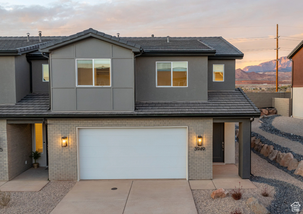View of front of property with brick siding, driveway, a garage, and stucco siding