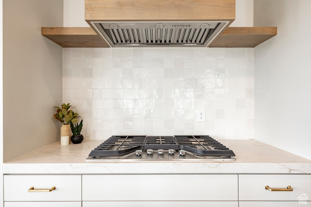 Kitchen with ventilation hood, stainless steel gas stovetop, tasteful backsplash, and white cabinetry