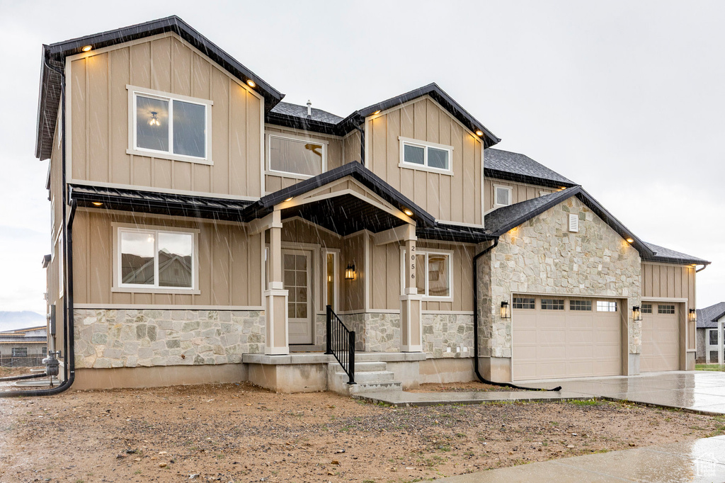 View of front of home featuring stone siding, board and batten siding, driveway, a garage, and roof with shingles