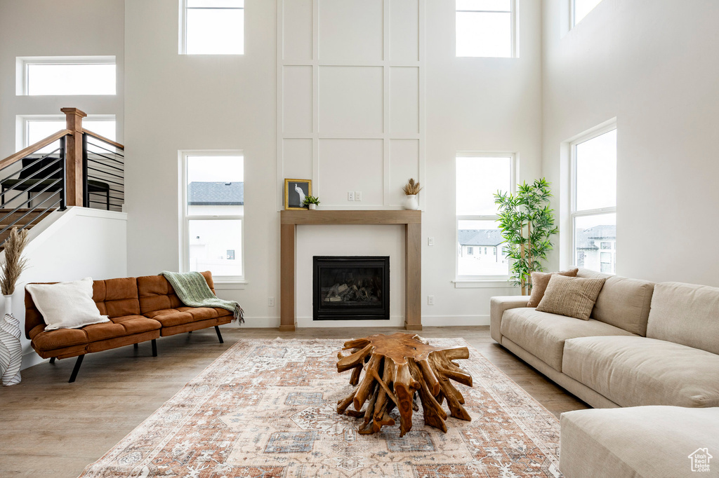 Living room featuring a high ceiling, a large fireplace, healthy amount of natural light, and wood finished floors