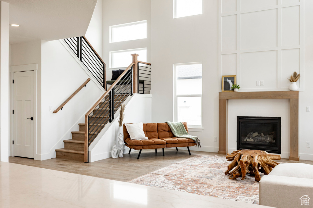 Living area with a high ceiling, healthy amount of natural light, stairs, a fireplace, and wood finished floors