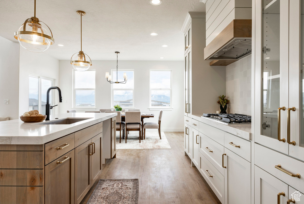 Kitchen featuring custom exhaust hood, light wood-type flooring, stainless steel gas stovetop, glass insert cabinets, and recessed lighting