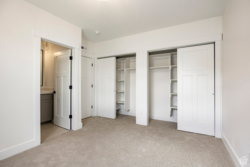 Unfurnished bedroom featuring light carpet, two closets, and ensuite bath