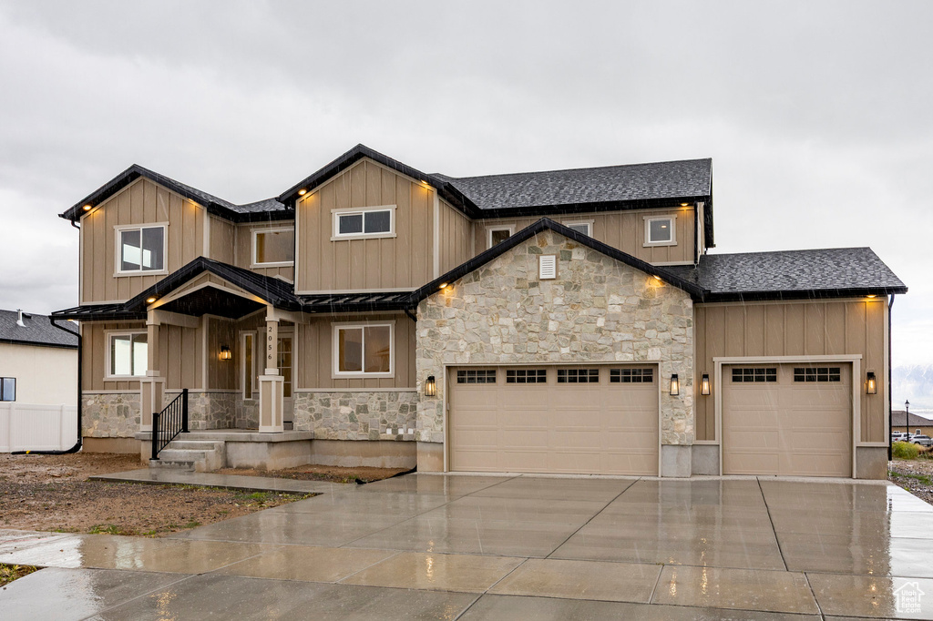 Craftsman house featuring driveway, stone siding, a garage, board and batten siding, and roof with shingles