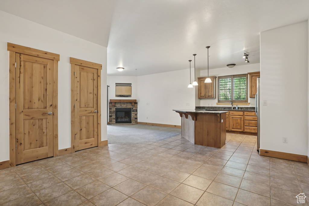 Kitchen featuring open floor plan, a breakfast bar, light tile patterned flooring, a stone fireplace, and decorative light fixtures