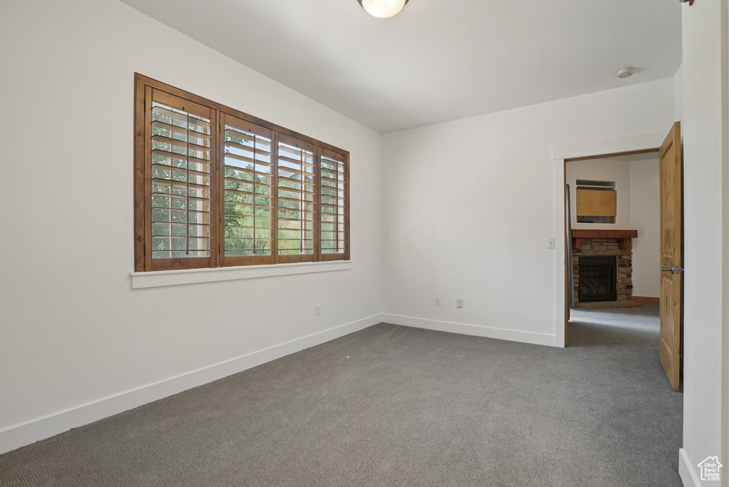 Empty room with a fireplace, dark colored carpet, and a smoke detector
