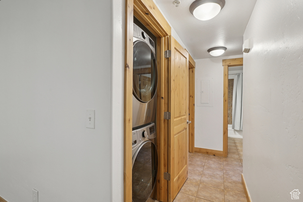 Washroom featuring stacked washer / drying machine, light tile patterned floors, and electric panel