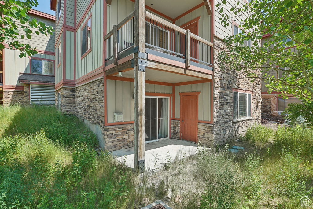 Doorway to property featuring stone siding, board and batten siding, a balcony, and a patio area
