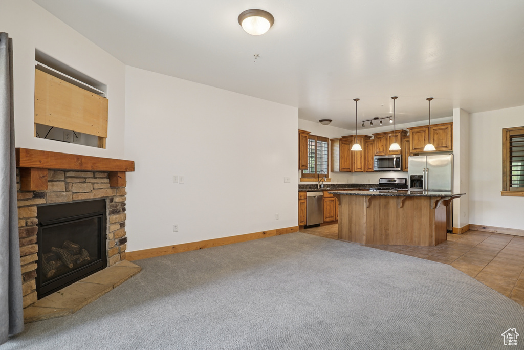 Kitchen featuring appliances with stainless steel finishes, a kitchen breakfast bar, a kitchen island, decorative light fixtures, and a fireplace