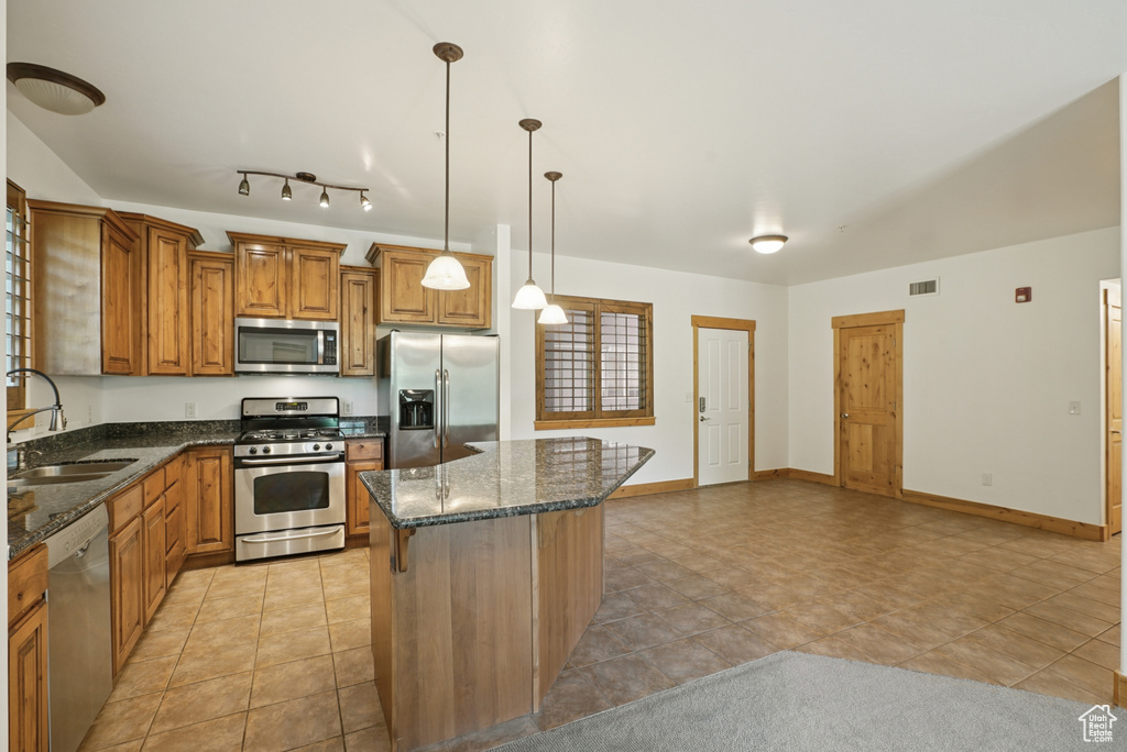 Kitchen with stainless steel appliances, brown cabinets, a center island, dark stone counters, and hanging light fixtures