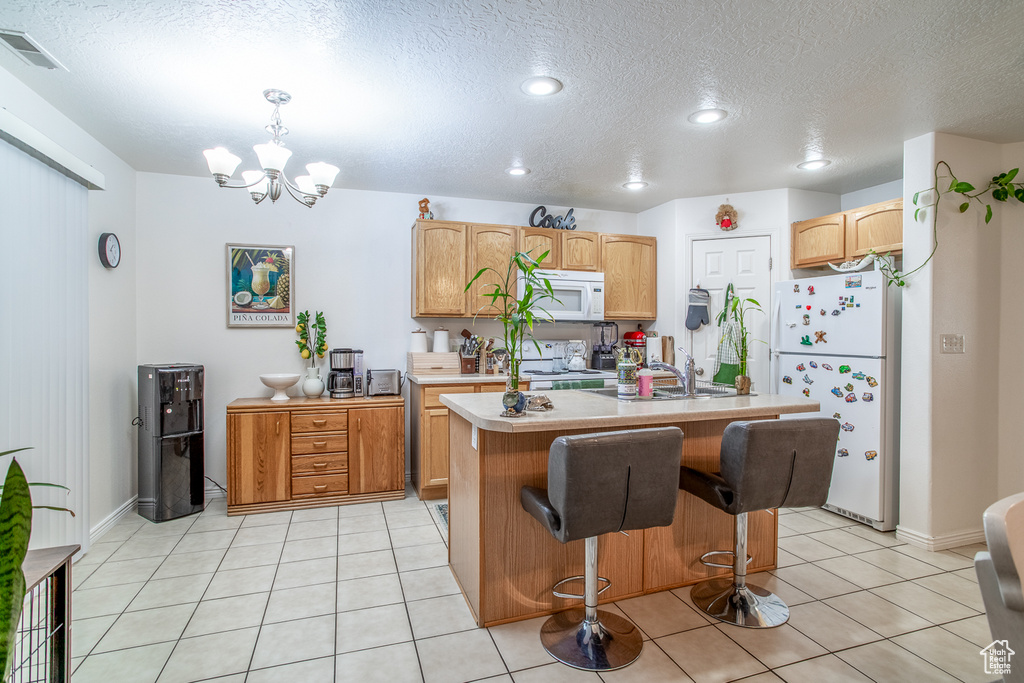 Kitchen featuring white appliances, light countertops, a chandelier, a textured ceiling, and a kitchen island