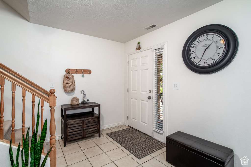 Foyer entrance with light tile patterned floors, stairway, and a textured ceiling