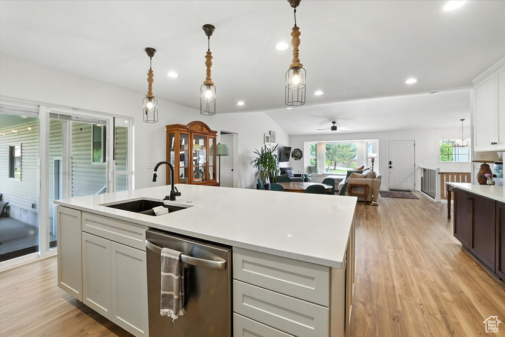 Kitchen with stainless steel dishwasher, light countertops, light wood-style floors, an island with sink, and decorative light fixtures