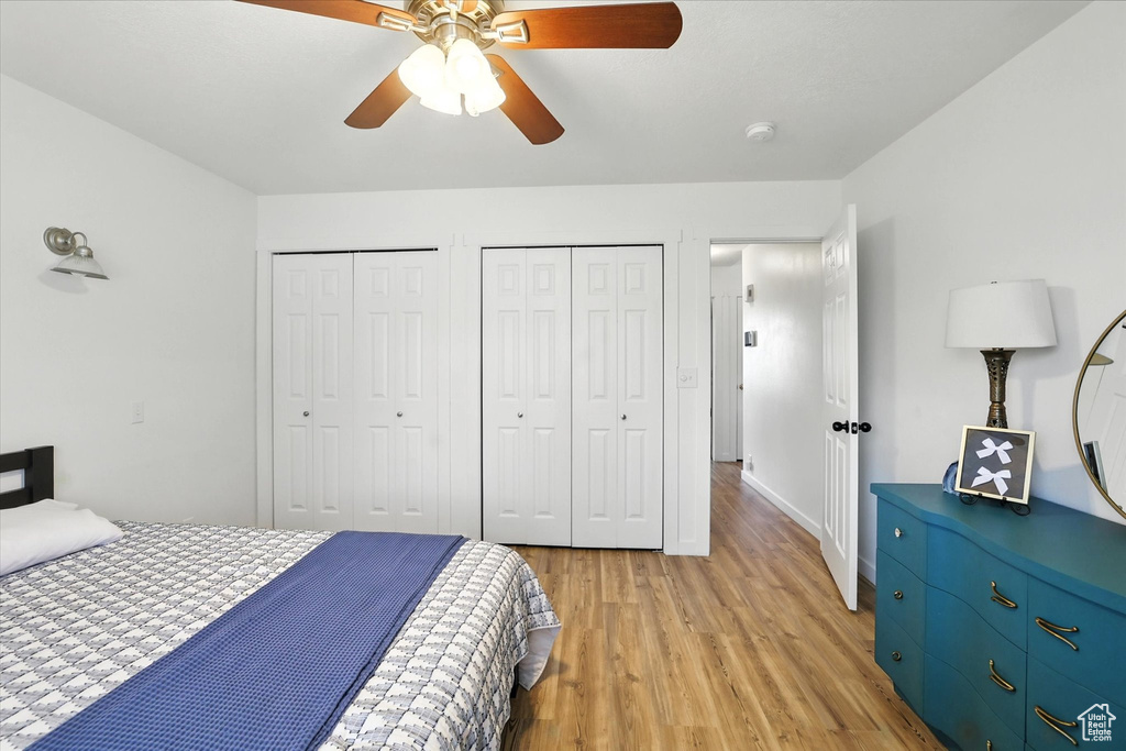 Bedroom with multiple closets, light wood-type flooring, and a ceiling fan