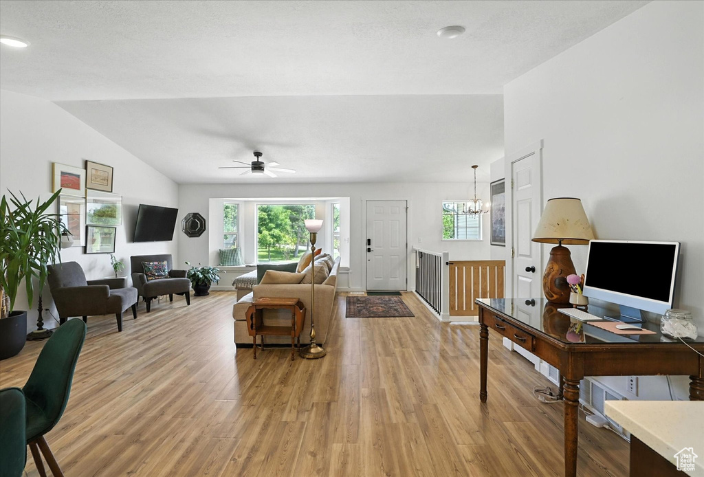 Living room featuring light wood-type flooring, vaulted ceiling, a chandelier, and a ceiling fan