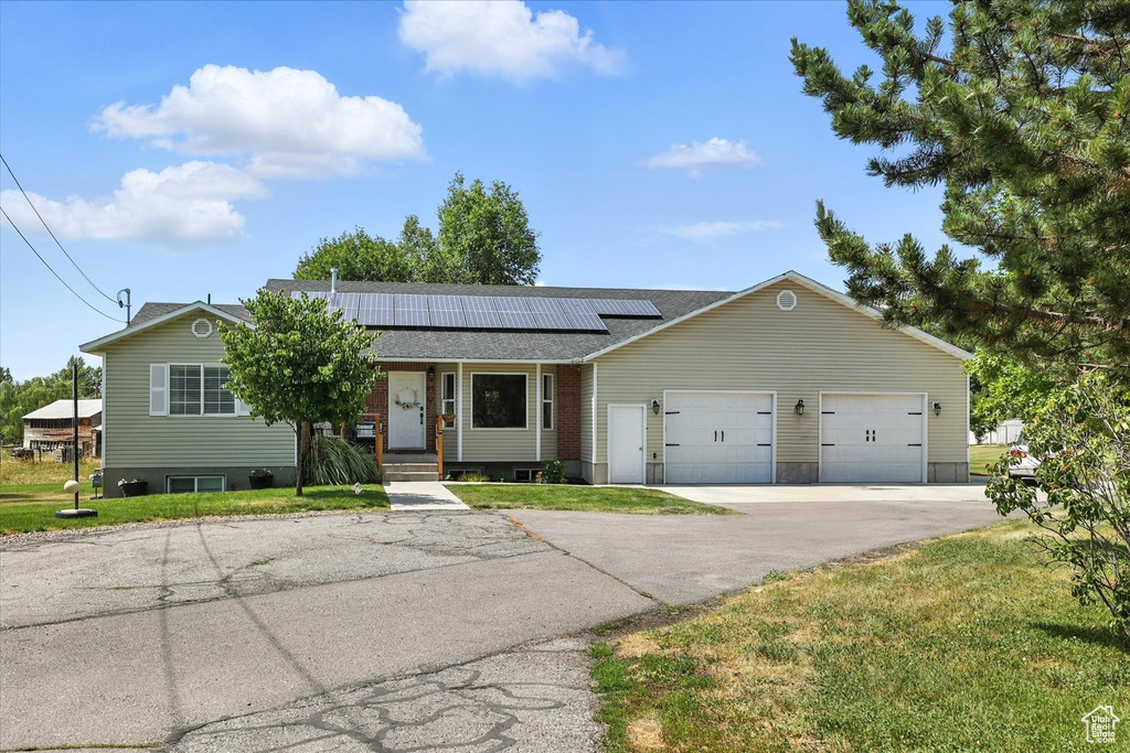 Ranch-style home featuring a front yard, roof mounted solar panels, an attached garage, and driveway
