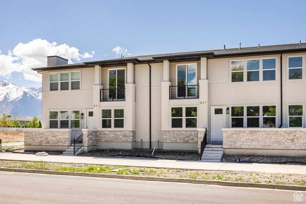 View of front of house featuring a balcony, stone siding, stucco siding, a mountain view, and entry steps