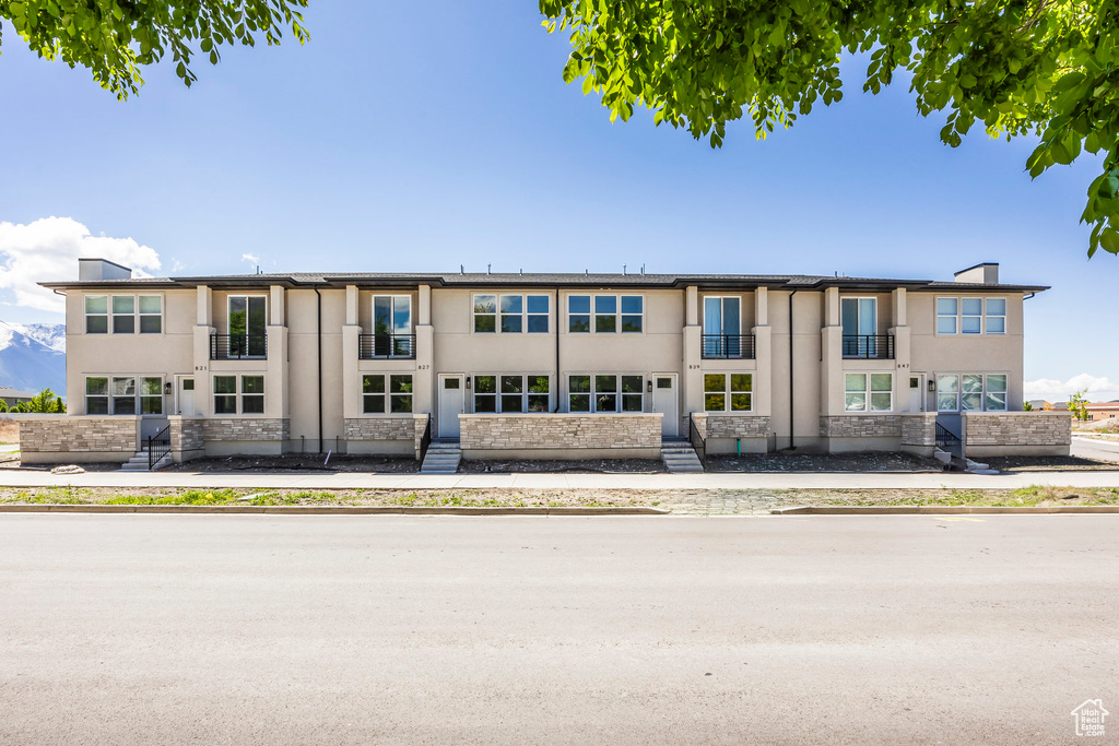 View of front of property with a balcony, stucco siding, and stone siding