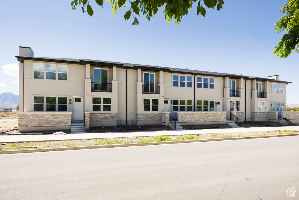 View of front of home featuring a balcony, stone siding, stucco siding, and entry steps