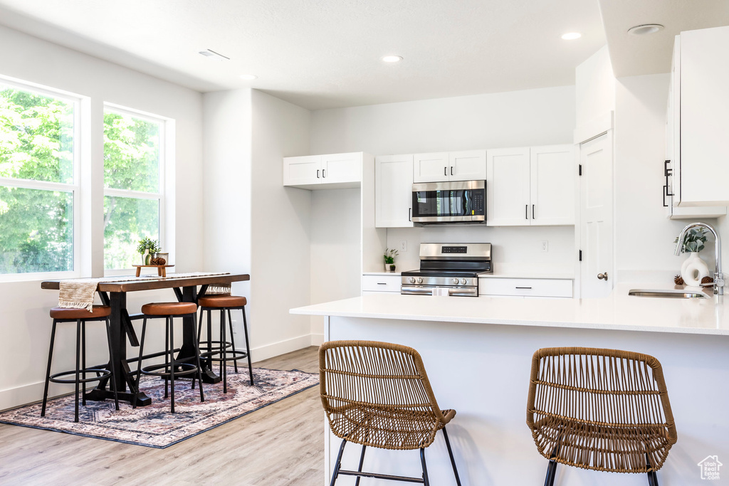 Kitchen with stainless steel appliances, light wood finished floors, plenty of natural light, white cabinetry, and recessed lighting