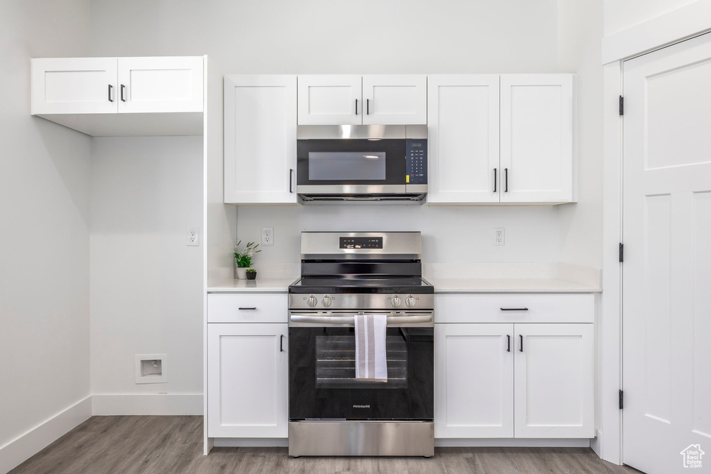 Kitchen with appliances with stainless steel finishes, white cabinetry, light countertops, and light wood finished floors