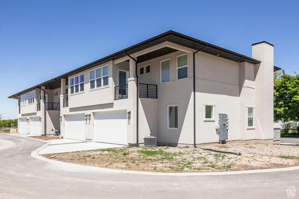 View of front of house with a garage, stucco siding, a balcony, and a chimney