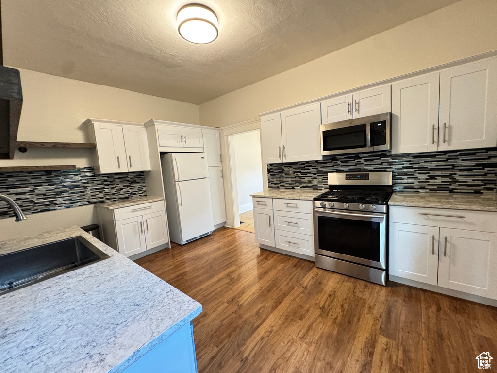 Kitchen featuring stainless steel appliances, decorative backsplash, white cabinets, dark wood finished floors, and a textured ceiling