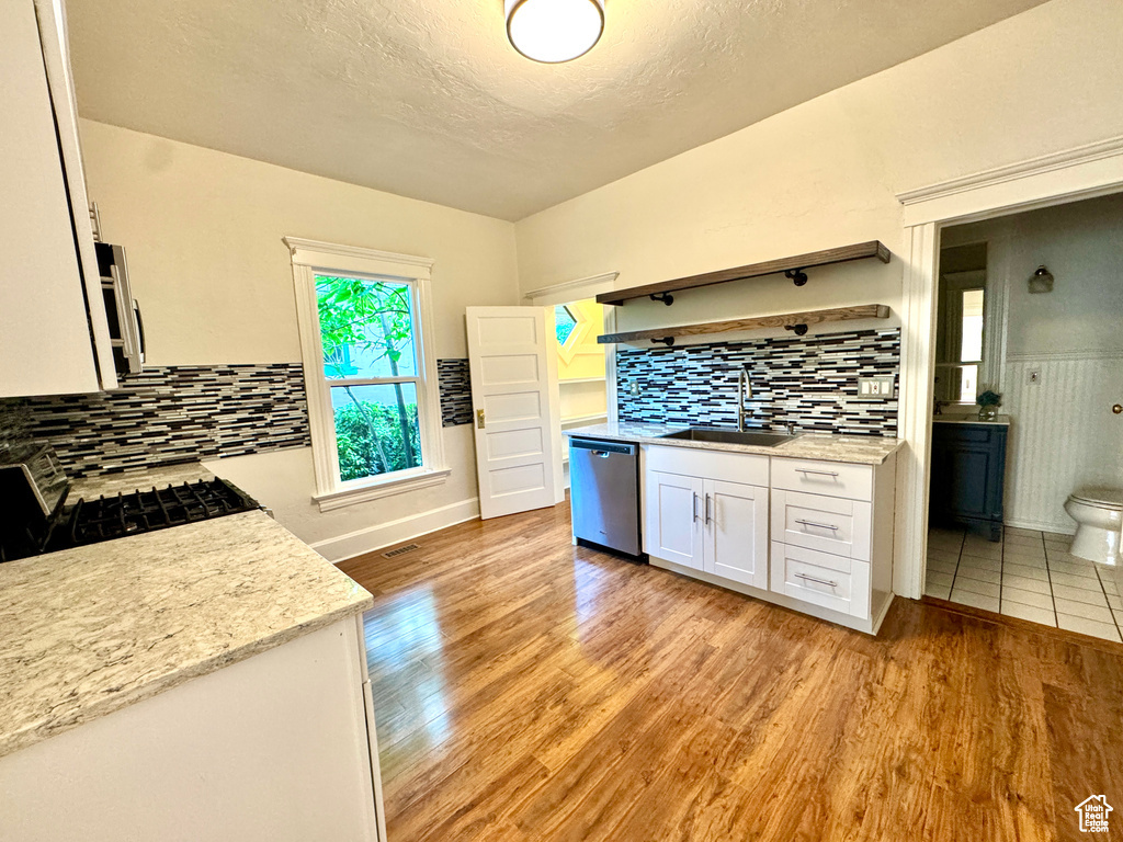 Kitchen featuring dishwasher, stove, white cabinets, light wood-style flooring, and tasteful backsplash