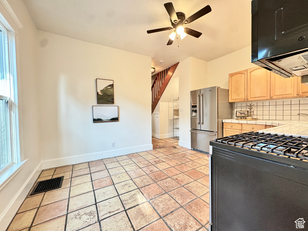 Kitchen featuring high end refrigerator, light brown cabinetry, black range with gas stovetop, tile counters, and exhaust hood