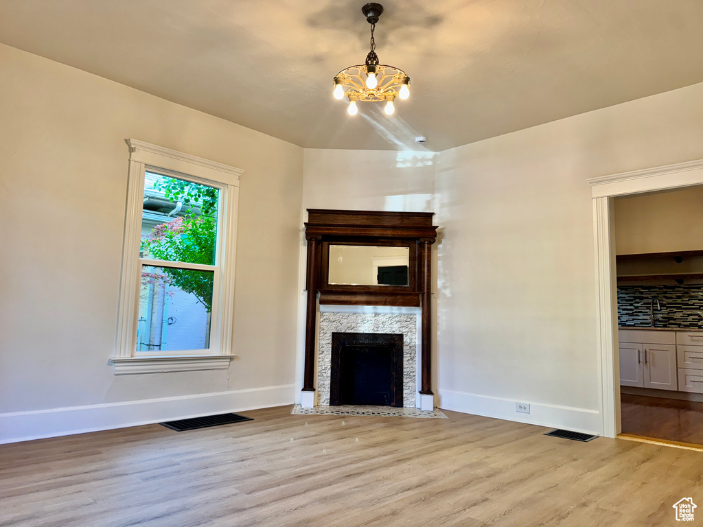 Unfurnished living room featuring a chandelier, light wood-style flooring, and a fireplace with flush hearth