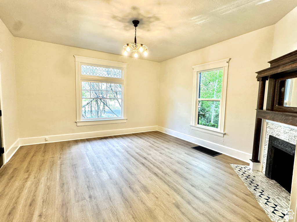 Unfurnished living room with wood finished floors, a chandelier, and a fireplace with flush hearth