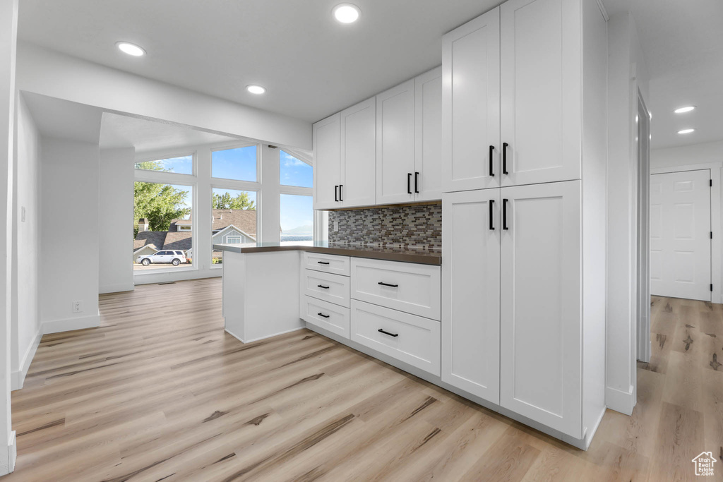 Kitchen featuring light wood-type flooring, white cabinets, backsplash, recessed lighting, and dark countertops