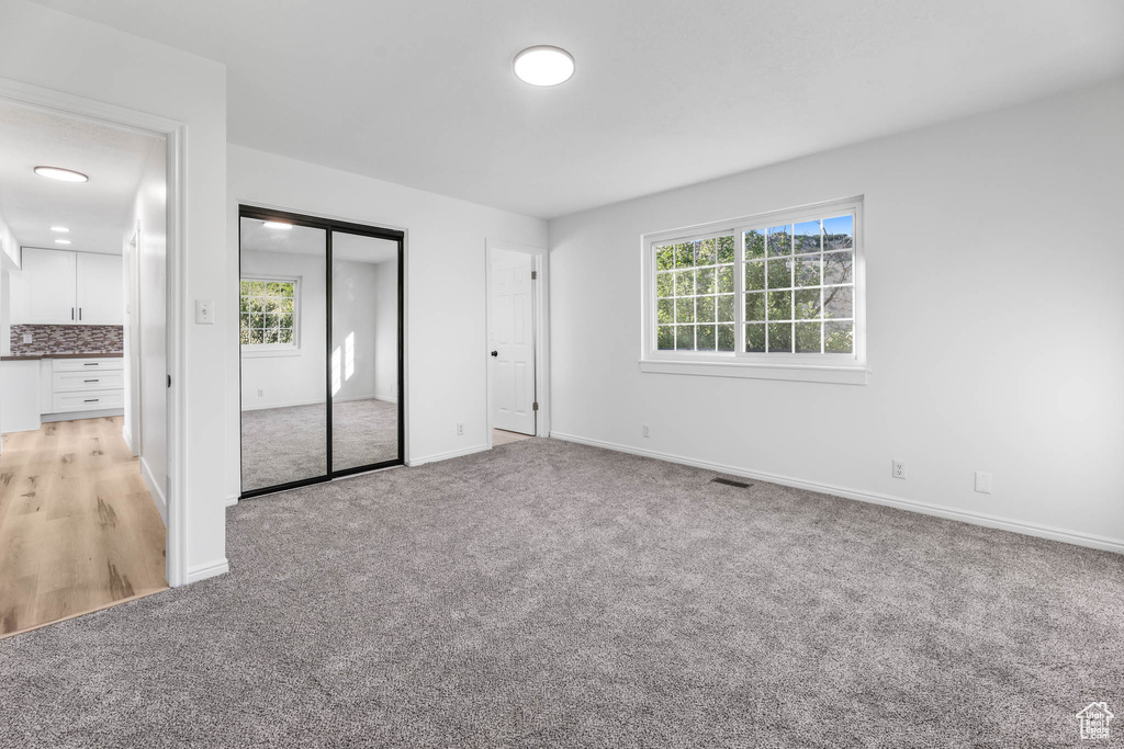 Unfurnished bedroom featuring light colored carpet, multiple windows, and a closet