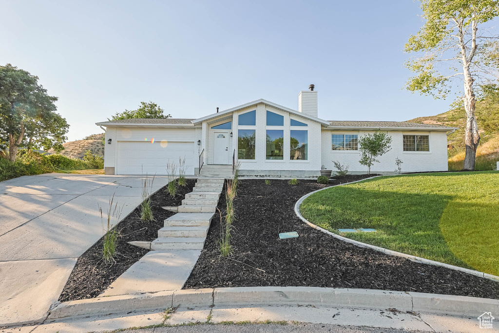 View of front of house with a chimney, a front lawn, concrete driveway, and a garage