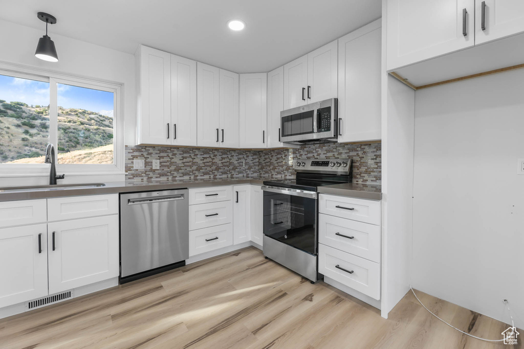 Kitchen featuring stainless steel appliances, light wood-style floors, white cabinetry, tasteful backsplash, and pendant lighting