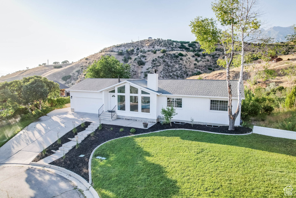 Ranch-style house with driveway, a mountain view, a chimney, a front yard, and an attached garage