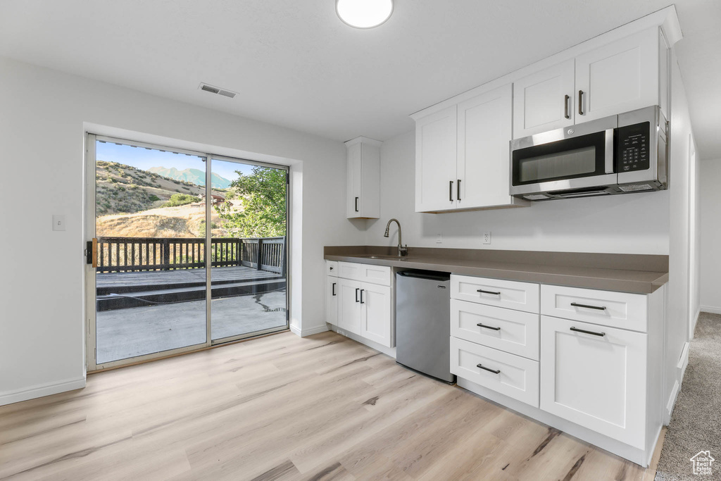 Kitchen featuring stainless steel appliances, dark countertops, white cabinets, and light wood-type flooring