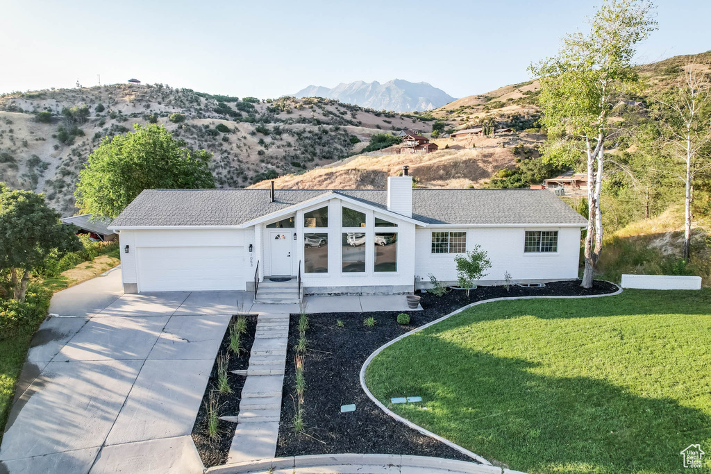 Ranch-style home with driveway, a front lawn, a mountain view, a chimney, and an attached garage