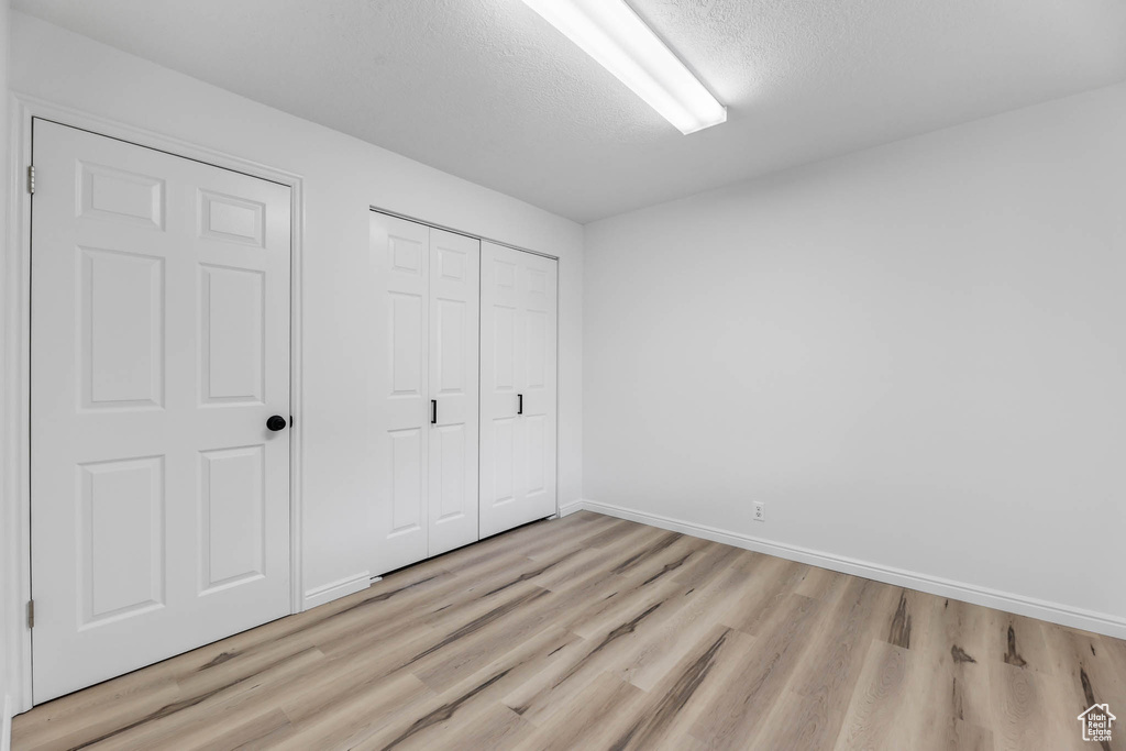 Unfurnished bedroom with light wood-style flooring, a closet, and a textured ceiling