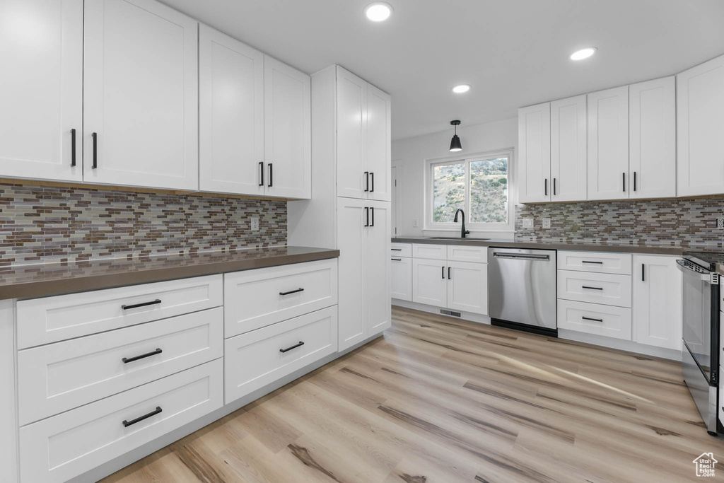 Kitchen with stainless steel appliances, dark countertops, light wood-style flooring, white cabinets, and recessed lighting