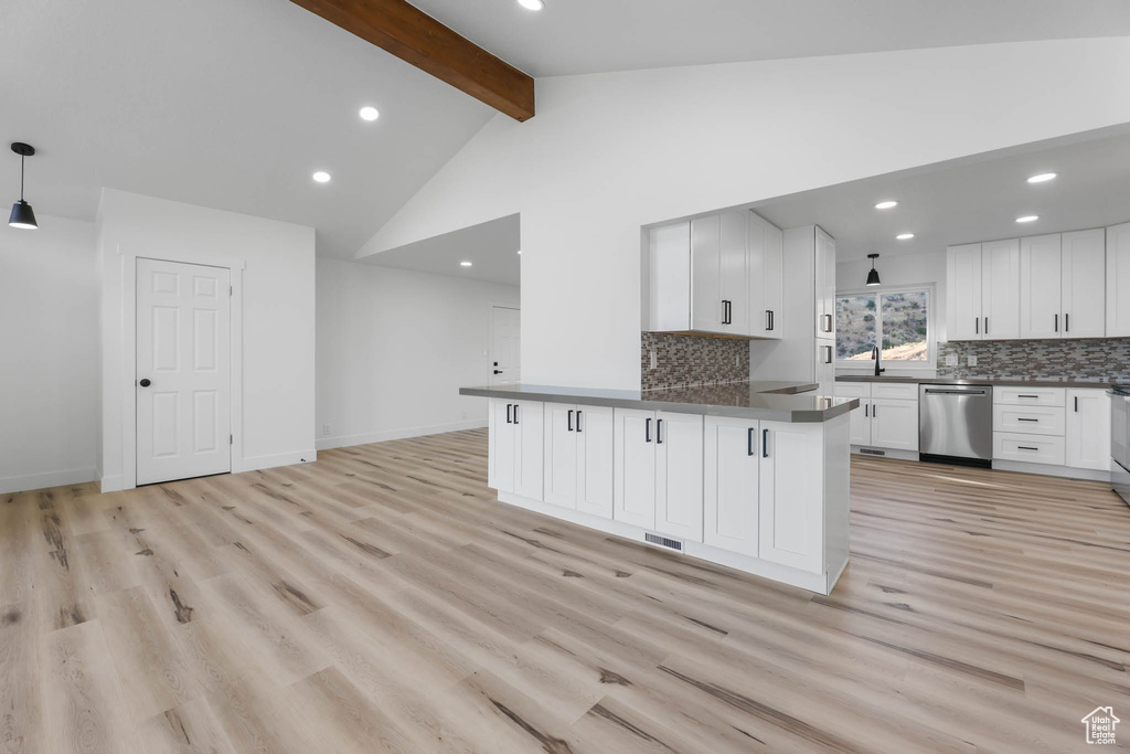 Kitchen featuring stainless steel dishwasher, dark countertops, beamed ceiling, backsplash, and white cabinetry