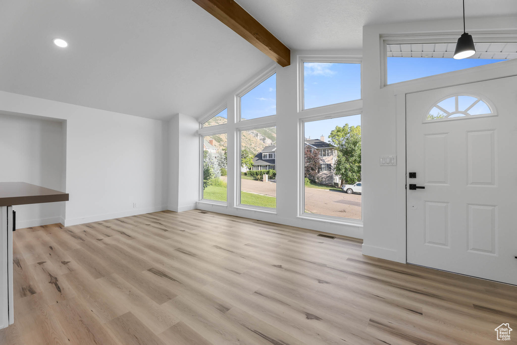 Unfurnished living room with healthy amount of natural light, beamed ceiling, light wood-style flooring, and high vaulted ceiling