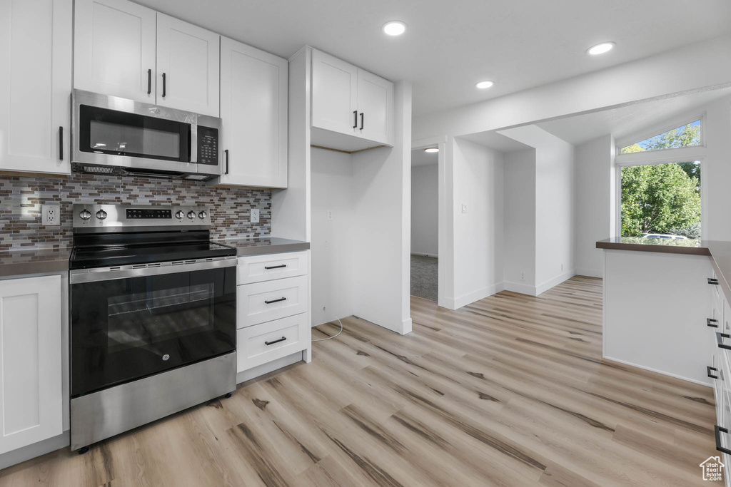 Kitchen with stainless steel appliances, white cabinetry, light wood finished floors, backsplash, and recessed lighting