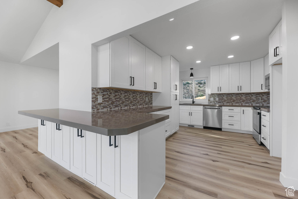 Kitchen featuring appliances with stainless steel finishes, a peninsula, dark countertops, tasteful backsplash, and white cabinetry