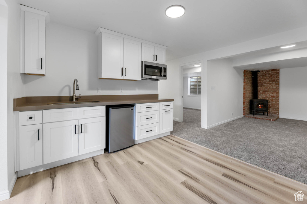 Kitchen with dishwasher, stainless steel microwave, a wood stove, dark countertops, and white cabinets
