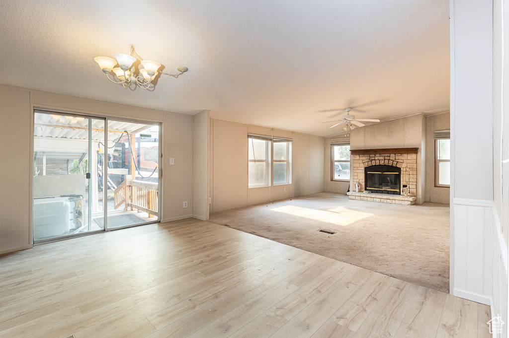 Unfurnished living room with a fireplace, a chandelier, a ceiling fan, and wood finished floors