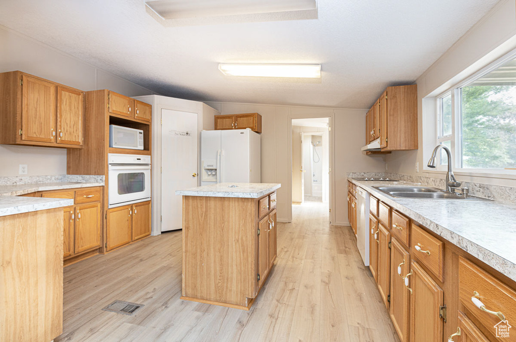 Kitchen featuring white appliances, light wood finished floors, a kitchen island, light countertops, and brown cabinetry
