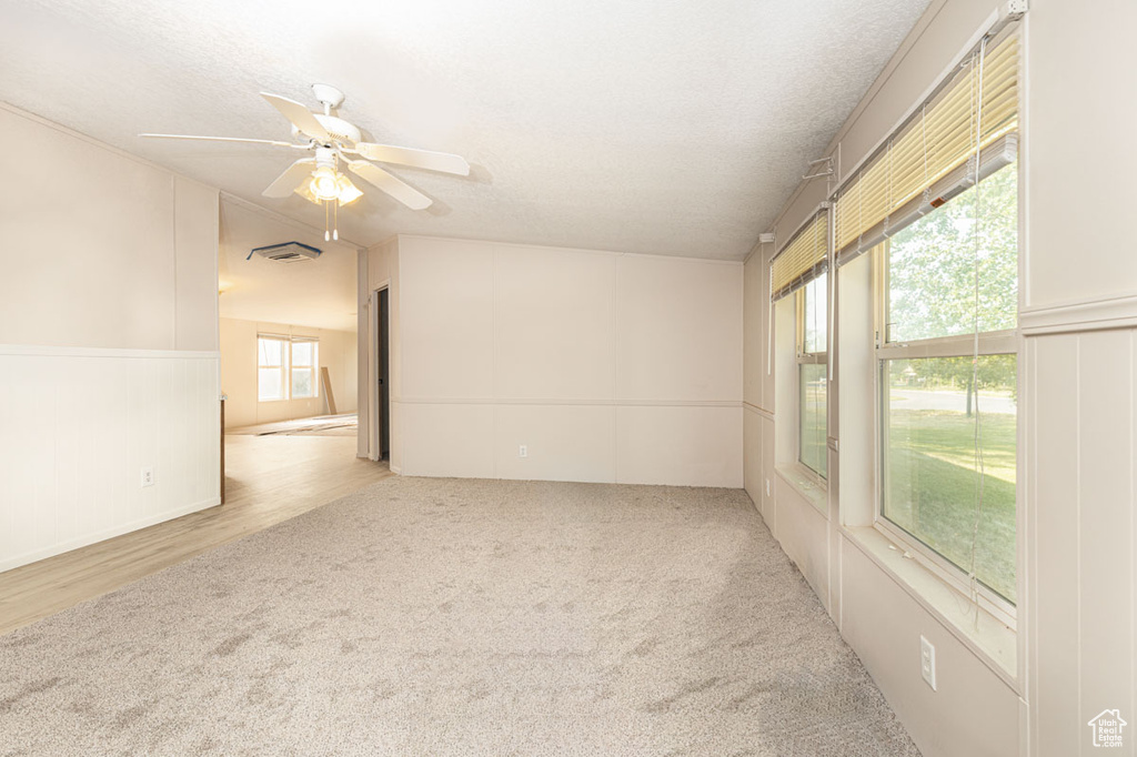 Empty room with carpet flooring, ceiling fan, wainscoting, and a textured ceiling